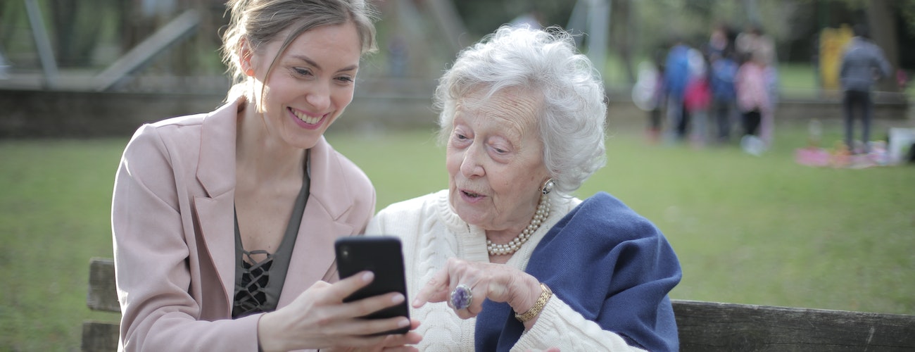 Junge Frau zeigt einer älteren Dame etwas auf dem Handy